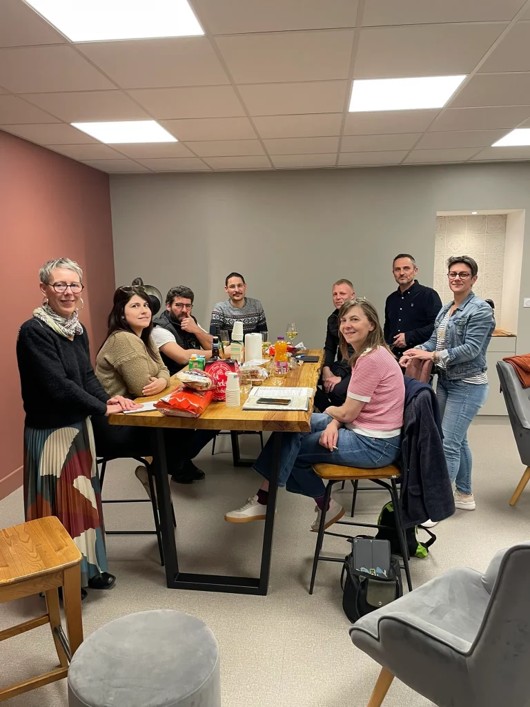 Une équipe de huit personnes discute autour d'une table en bois, des collations et boissons sont disposées dessus.