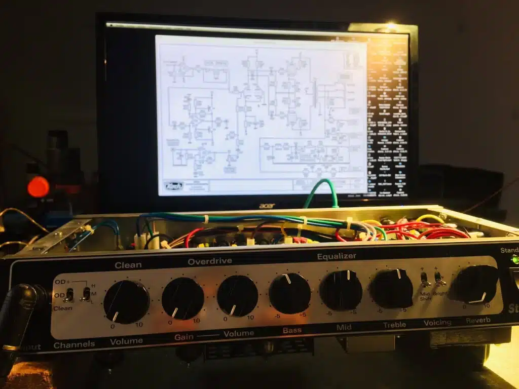 Amplificateur de musique ouvert, montrant les composants internes, avec un schéma électronique affiché sur un écran d'ordinateur Acer en arrière-plan.
