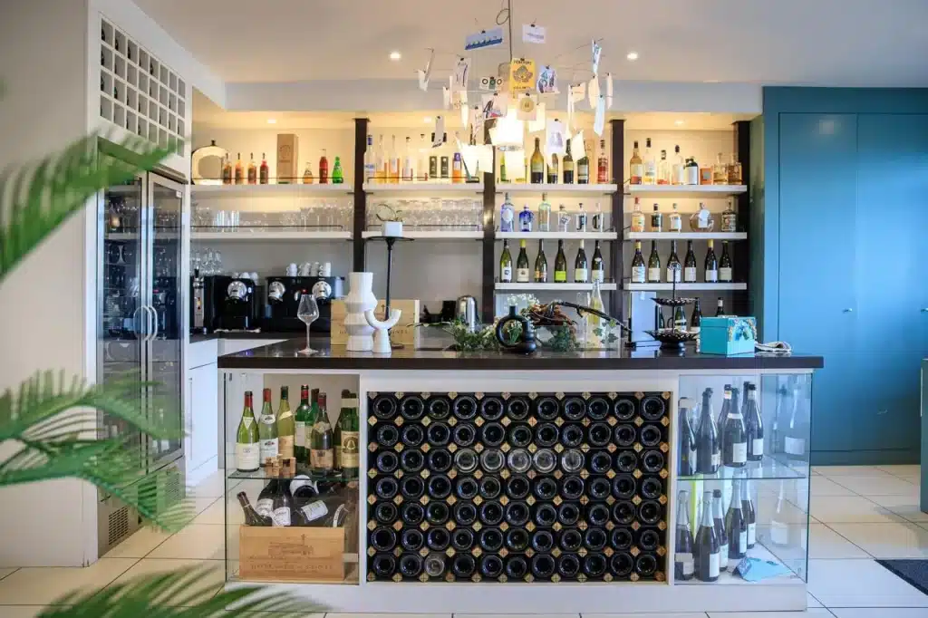 Bar design moderne avec présentoir à bouteilles, réfrigérateur à vin, étagères garnies de bouteilles et verres, et un buffet.