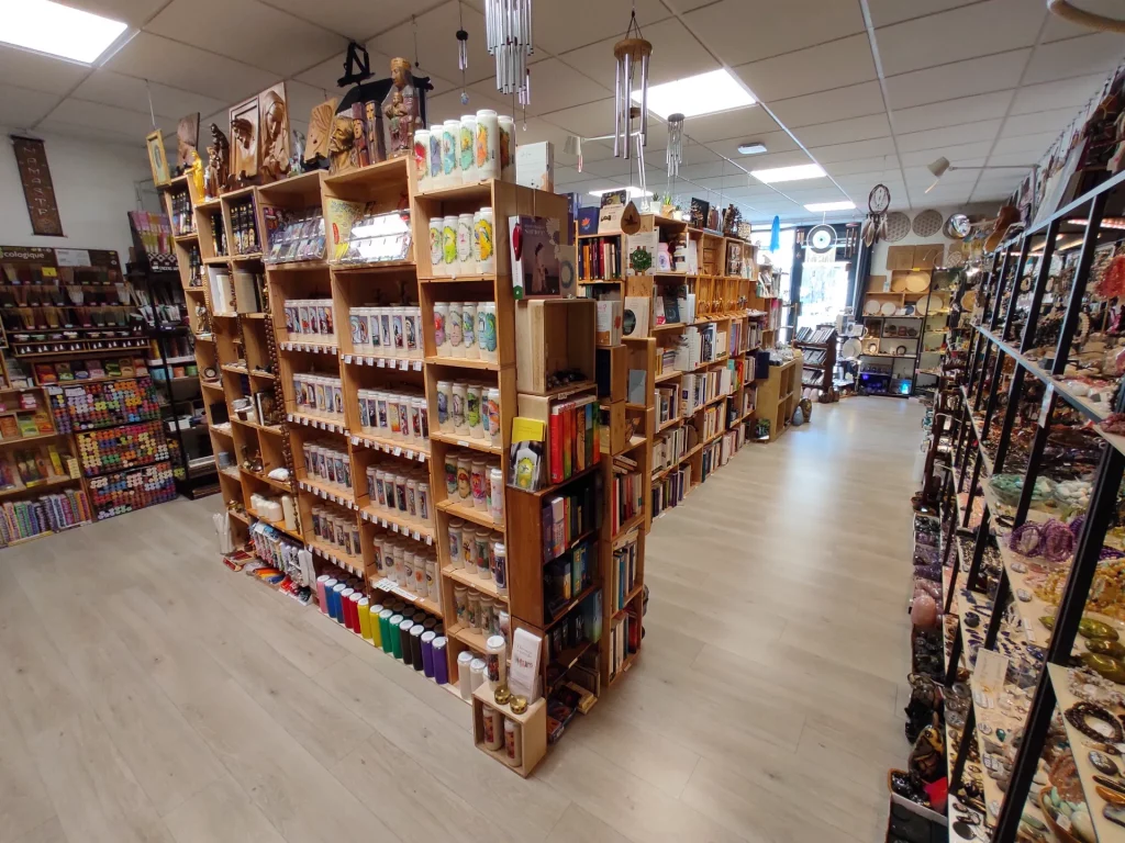 Intérieur d'une boutique remplie d'étagères en bois surchargées de livres, bougies, statuettes, carillons éoliens et autres articles de décoration et ésotériques.