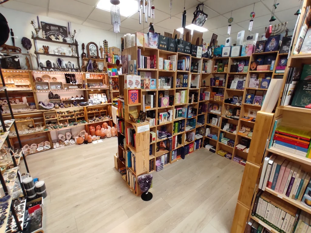 Intérieur d'une boutique proposant des livres, des cristaux et des objets ésotériques sur des étagères en bois.
