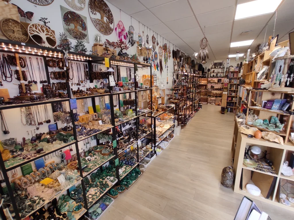 Vue d'ensemble d'une boutique d'articles spirituels et ésotériques, avec des étagères remplies de bijoux, pierres, attrape-rêves et décorations.