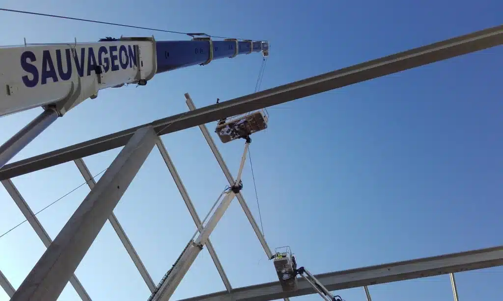 Mise en place de poutrelles métalliques sur un chantier par des nacelles élévatrices et une grue 'Sauvageon'.