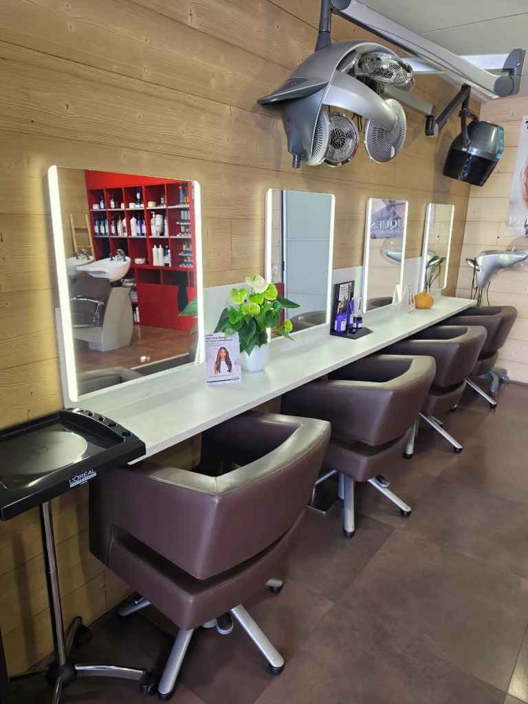 Intérieur de salon de coiffure avec chaises marron, longs miroirs éclairés, sèche-cheveux mural et étagères de produits.