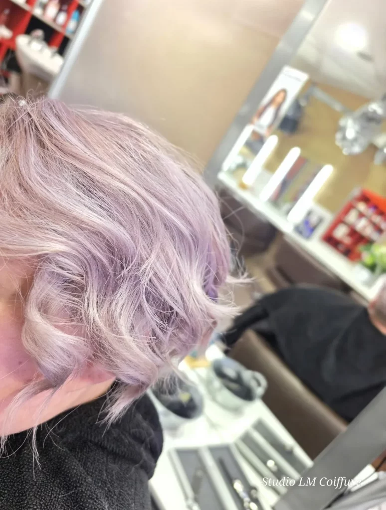 Coupe de cheveux courts dégradés avec des ondulations et une couleur lilas pastel, vue de côté.