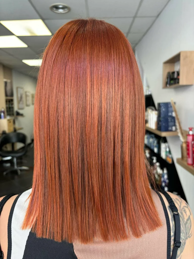 Vue arrière d'une chevelure mi-longue d'une couleur cuivre avec des reflets blonds et des pointes bien nettes.