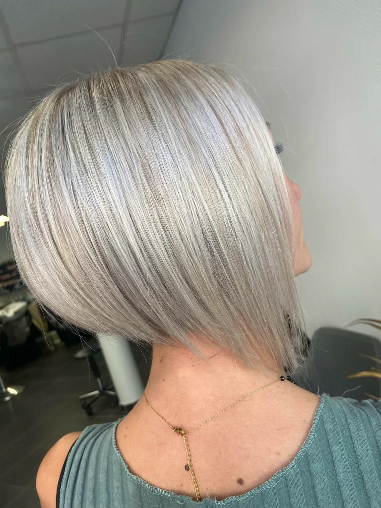 Vue arrière d'une femme avec une coupe dégradée courte d'un blond platine lumineux, aux reflets argentés.