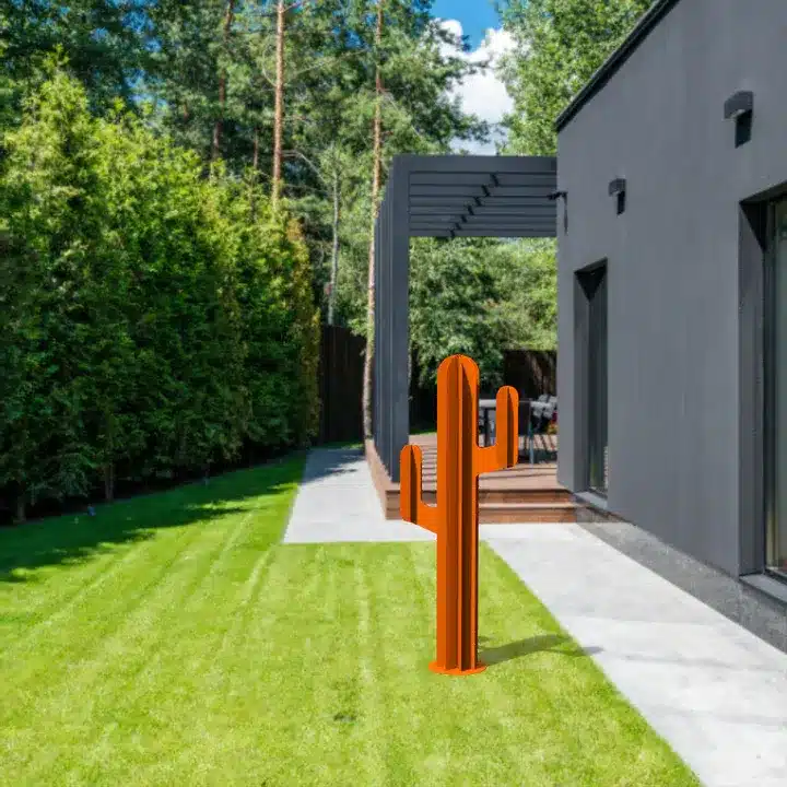 Décoration de jardin en forme de cactus stylisé de couleur orange vif, installée sur une pelouse impeccable à côté d'une terrasse.