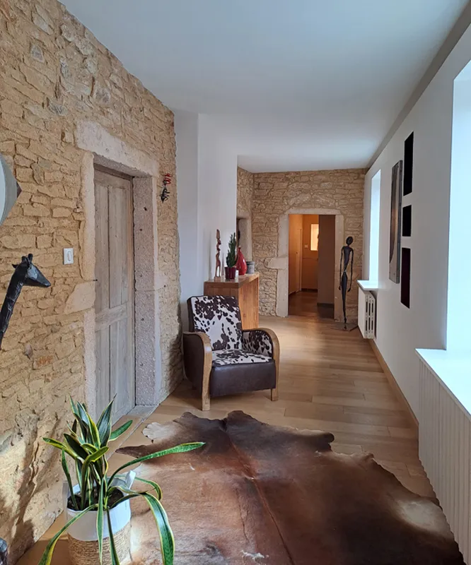 Couloir d'intérieur avec mur en pierre, fauteuil en cuir et motif vache, tapis en peau de bête et sol en bois verni.