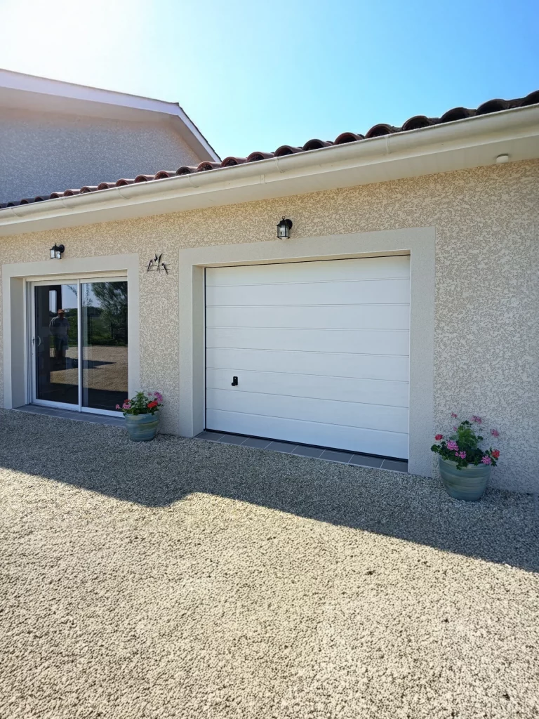 Façade d'une maison avec une porte de garage blanche à sections horizontales et une porte coulissante vitrée.