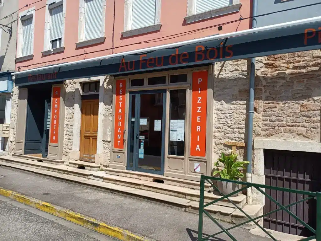 Façade du restaurant "Au Feu de Bois" proposant des plats à emporter et une pizzeria-traiteur, avec un passage piéton devant.
