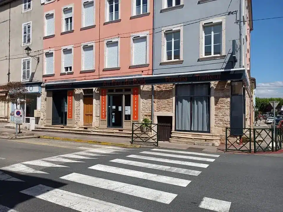 Façade du restaurant-pizzeria Au Feu de Bois avec ses enseignes 'Restaurant', 'À Emporter' et 'Pizzeria' sur fond de murs en pierre et de façade rose.
