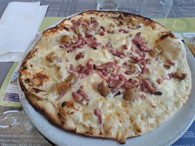 Tarte flambée garnie de lardons, de pommes de terre et de fromage fondant sur une pâte fine et croustillante.