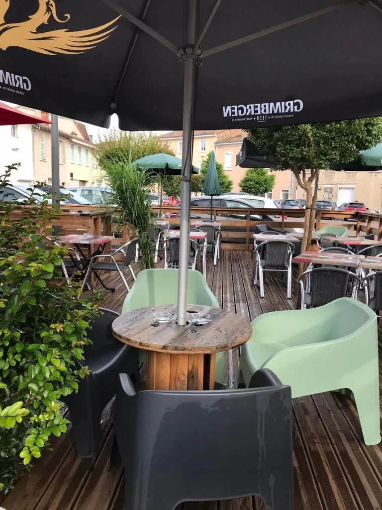 Terrasse extérieure d'un restaurant avec des tables, des chaises, des parasols et de la végétation.