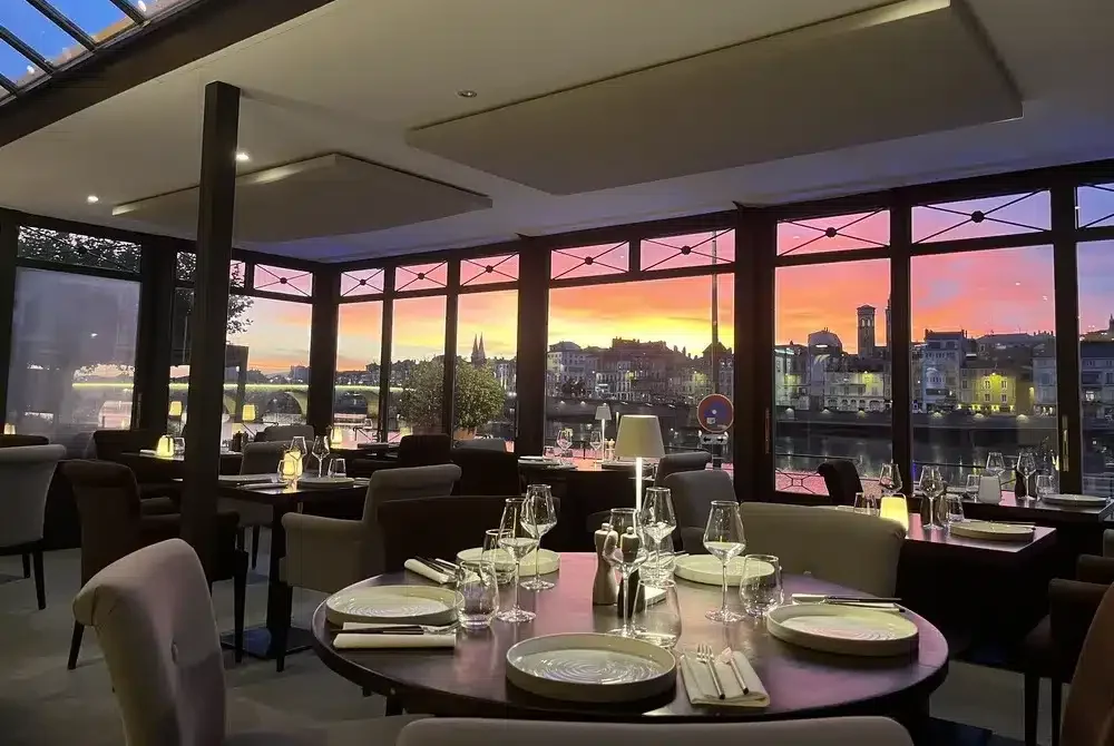 Tables dressées dans un restaurant avec une vue panoramique sur une ville et un coucher de soleil spectaculaire.
